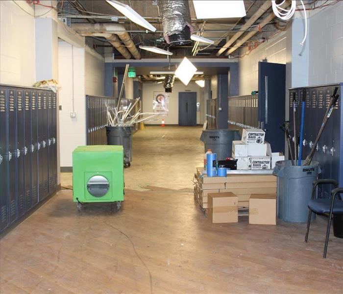 blue lockers in a hallway with HEPA filters and Air movers, ceiling tiles are missing, floor is brown