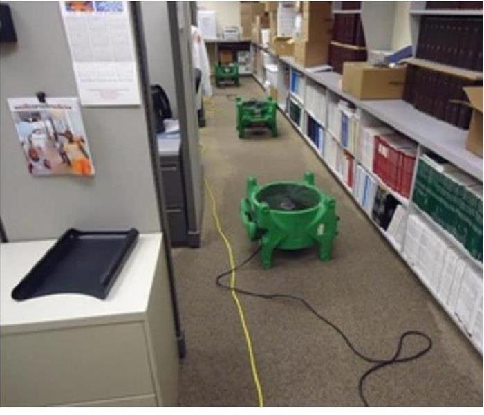 office building, gray carpeted floors, green SERVPRO air movers on the ground, shelves and cabinets on the sides of the aisle