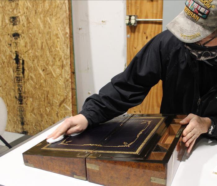 SERVPRO veteran wiping a brown writing desk after fire damage in contents repair warehouse