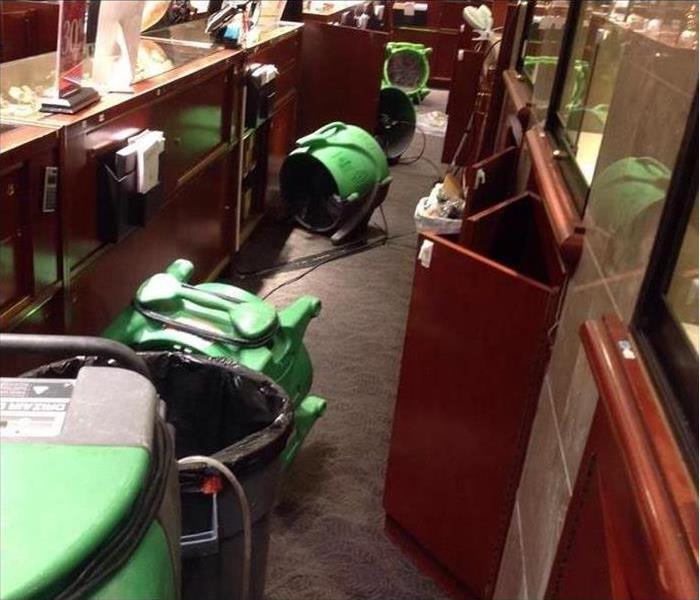 behind a jewelry counter, cabinet doors open, SERVPRO green air movers on the ground airing the area out