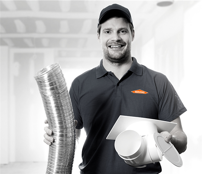 SERVPRO male technician holding piece of duct work staring at the camera and smiling, black and white image